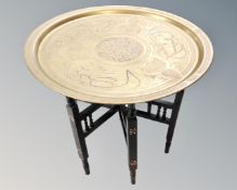 A circular eastern brass topped table on folding base,