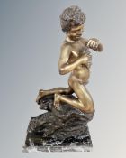 A bronze figure of a fishing boy kneeling on a rock