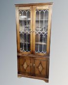 A pair of double leaded glass door corner cabinets fitted with cupboards below, in an oak finish.