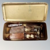 A tin containing a collection of pocket knives and hunting knives in sheathes.