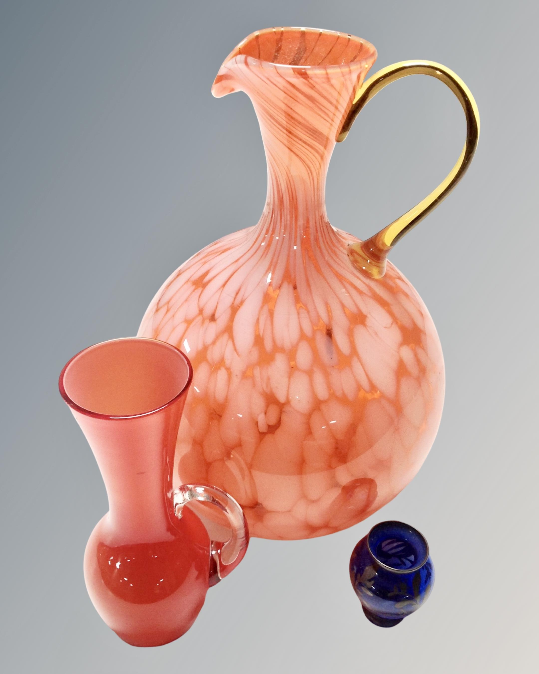 A tangerine art glass jug together with two further glass vases.