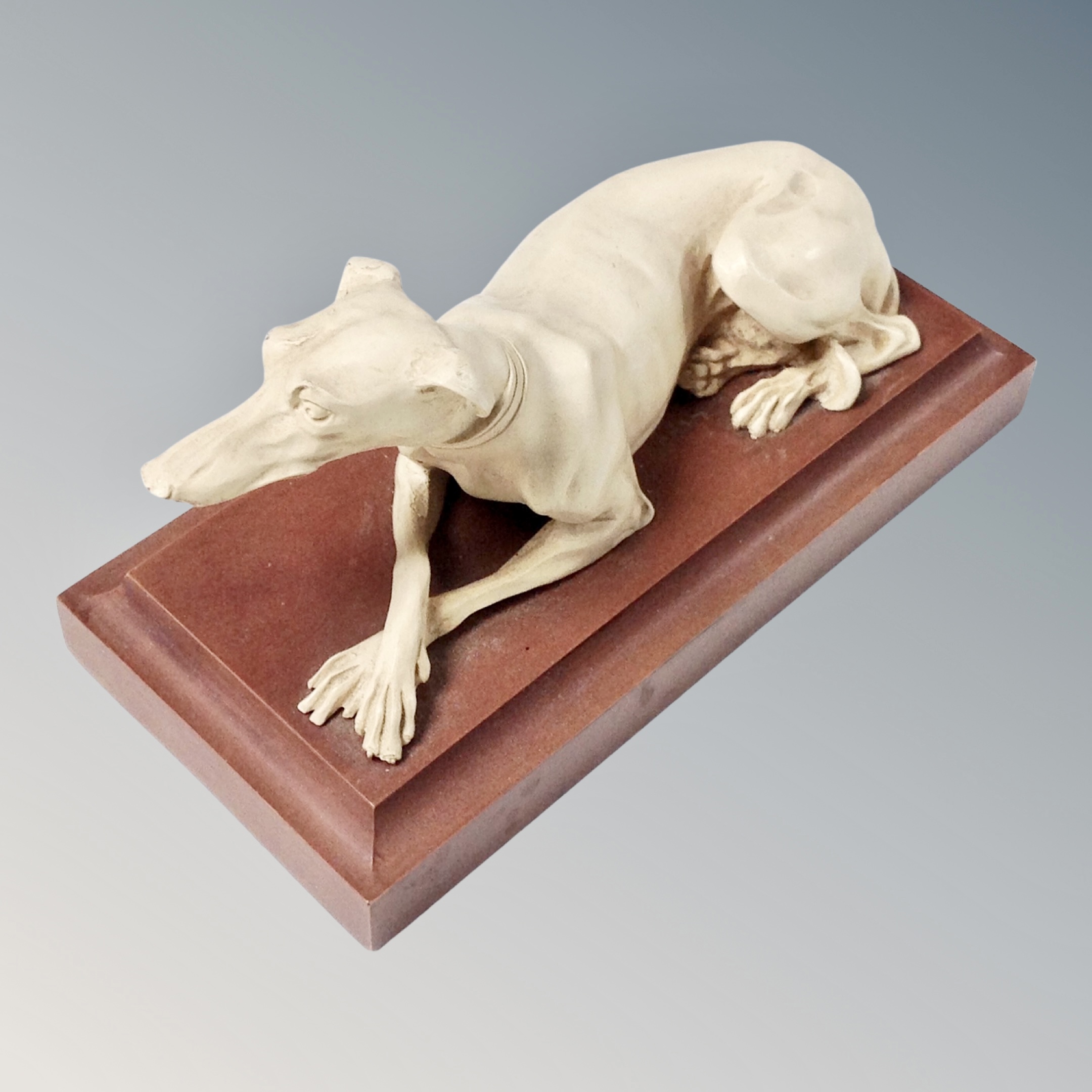 A composition figure of a greyhound resting on a wooden plinth, marked made in Great Britain.