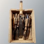 A wooden caddy containing vintage woodworking chisels, various sizes.