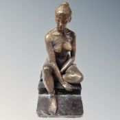 A large heavy bronzed figure of a nude lady sitting on a pedestal.