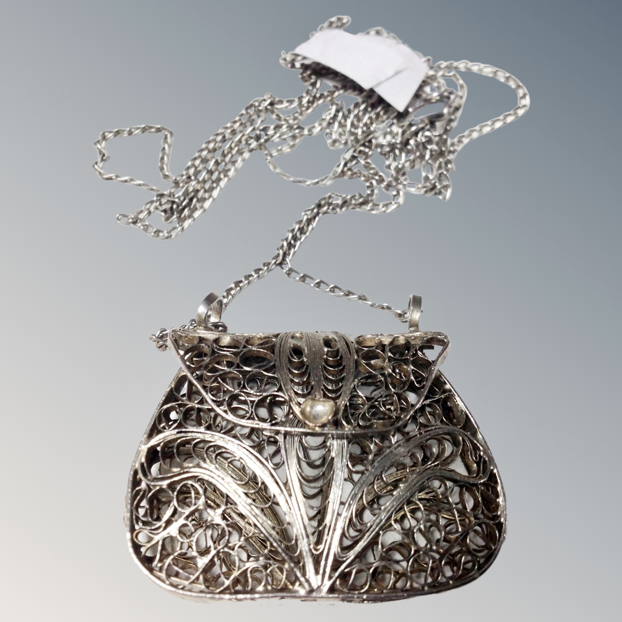 A white metal miniature handbag on chain, possibly used as a vinaigrette.