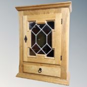 A Scandinavian blond oak wall cabinet with leaded glass doors and drawer.