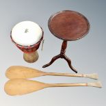 An occasional table together with a hand drum and a pair of paddle oars.