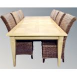 A contemporary extending dining table with two leaves in an oak finish with a set of eight wicker