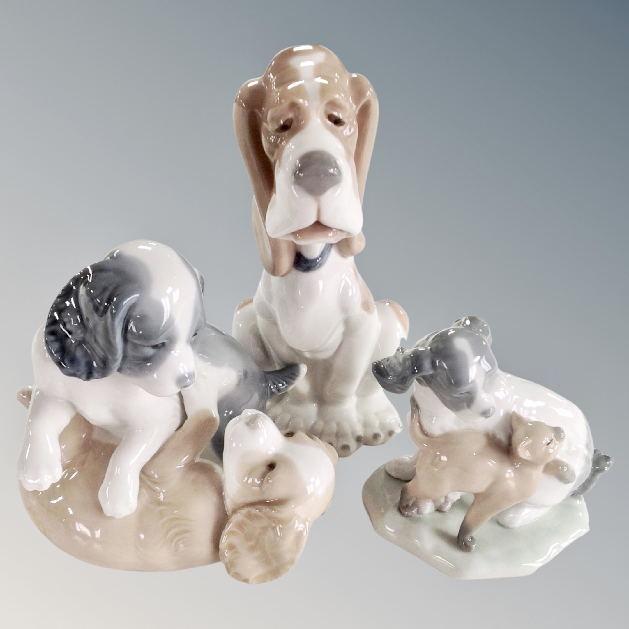 A Nao figure of a seated hound together with two further Nao figure groups, playful puppies.