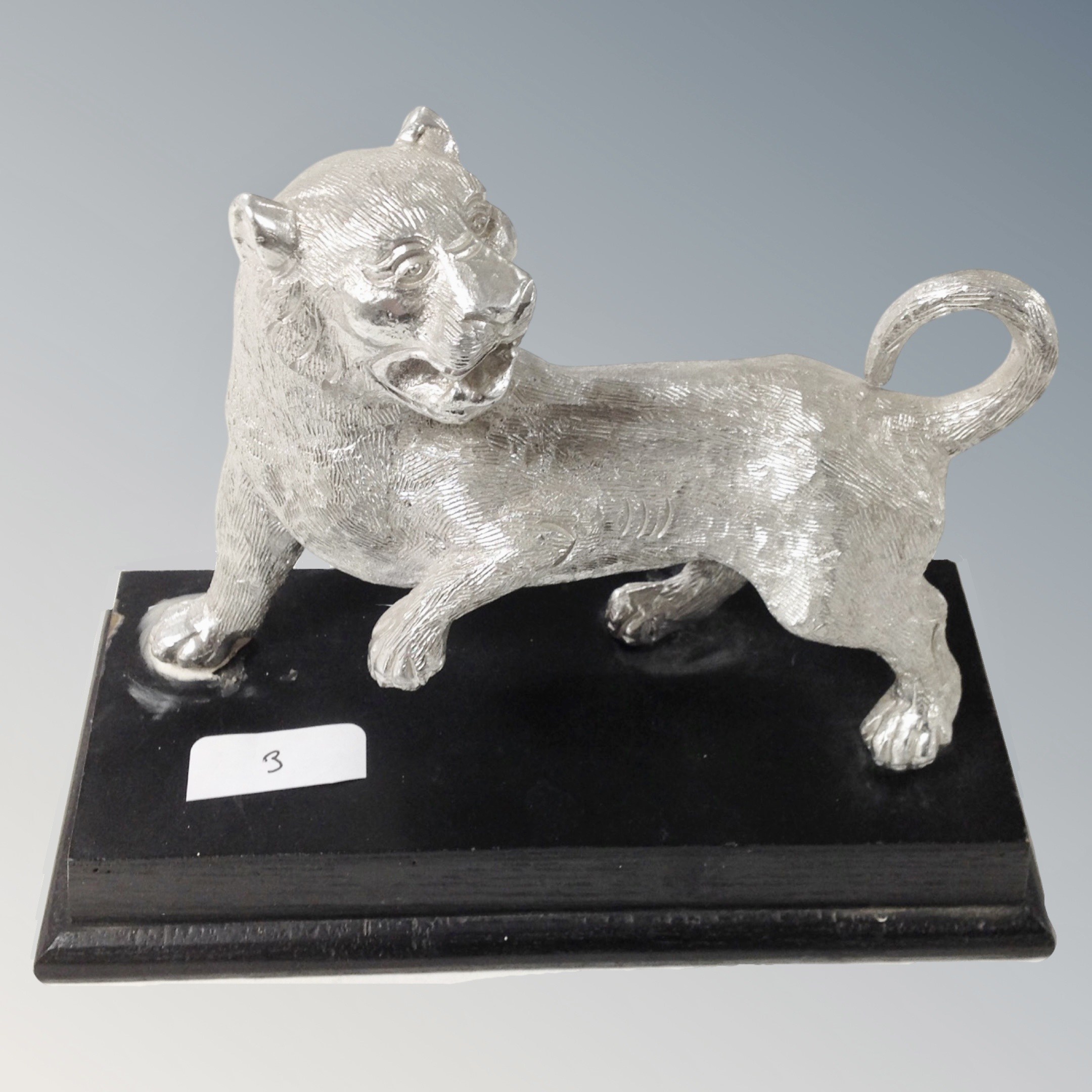 A white metal sculpture of a tiger on plinth