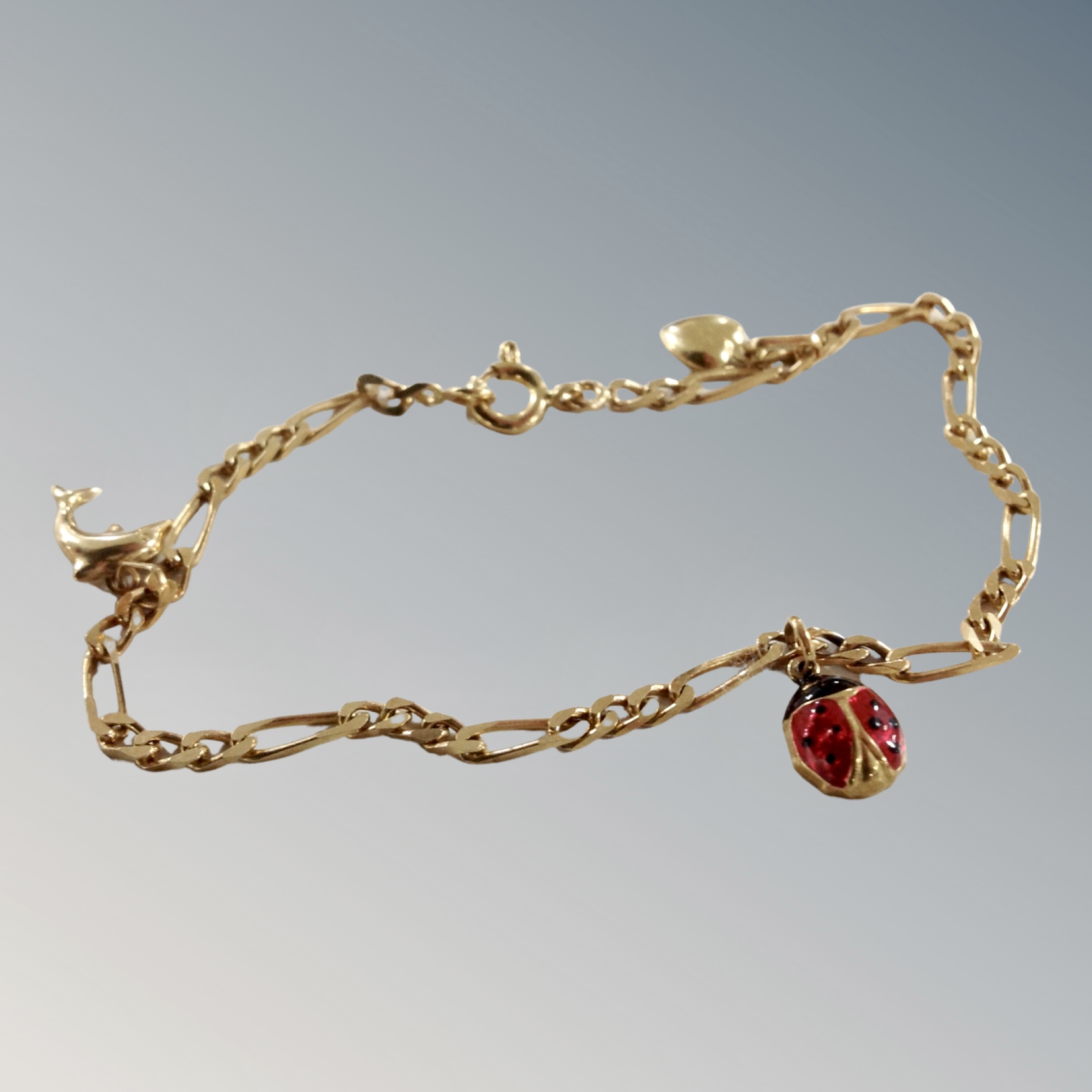 An 18ct gold charm bracelet with charms of ladybird, heart and dolphin, 4g.