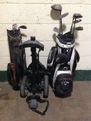 A collection of golf clubs, two golf bags and a caddy.