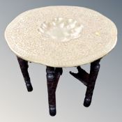 An embossed brass table on folding carved table base