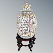 A Portuguese ceramic lidded vase on an oriental style wooden stand.