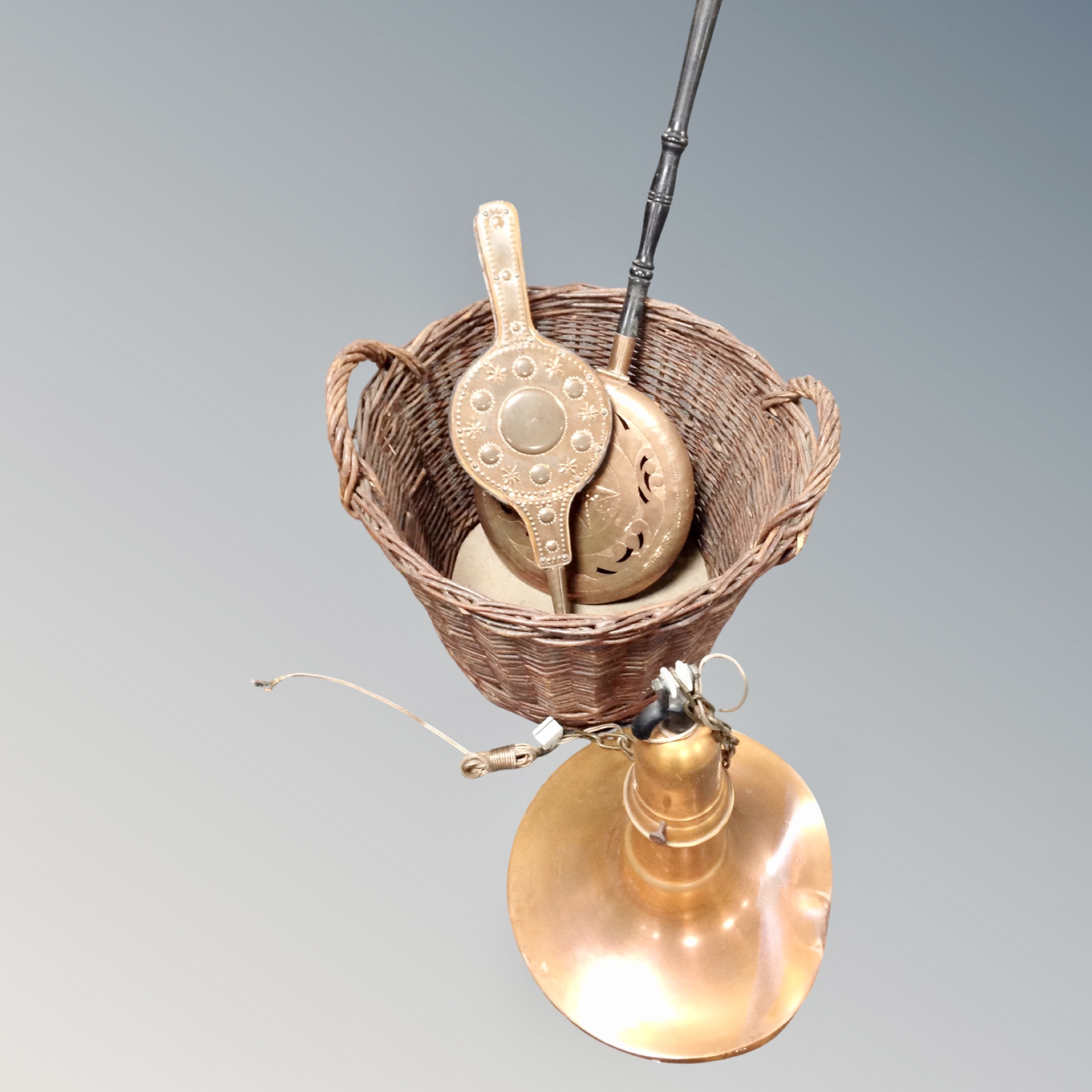 A retro style copper light fitting together with a wicker log basket containing brass beech-handled