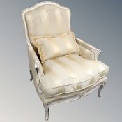 A cream and gilt French armchair upholstered in a striped fabric, with cushion.