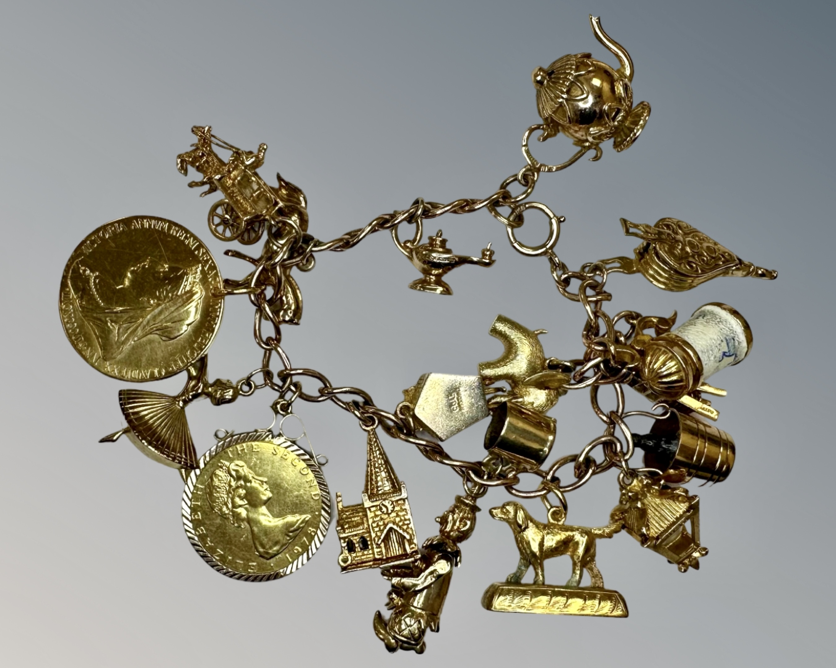 A 9ct gold charm bracelet set with many charms and two silver-gilt coins, 69.6g.