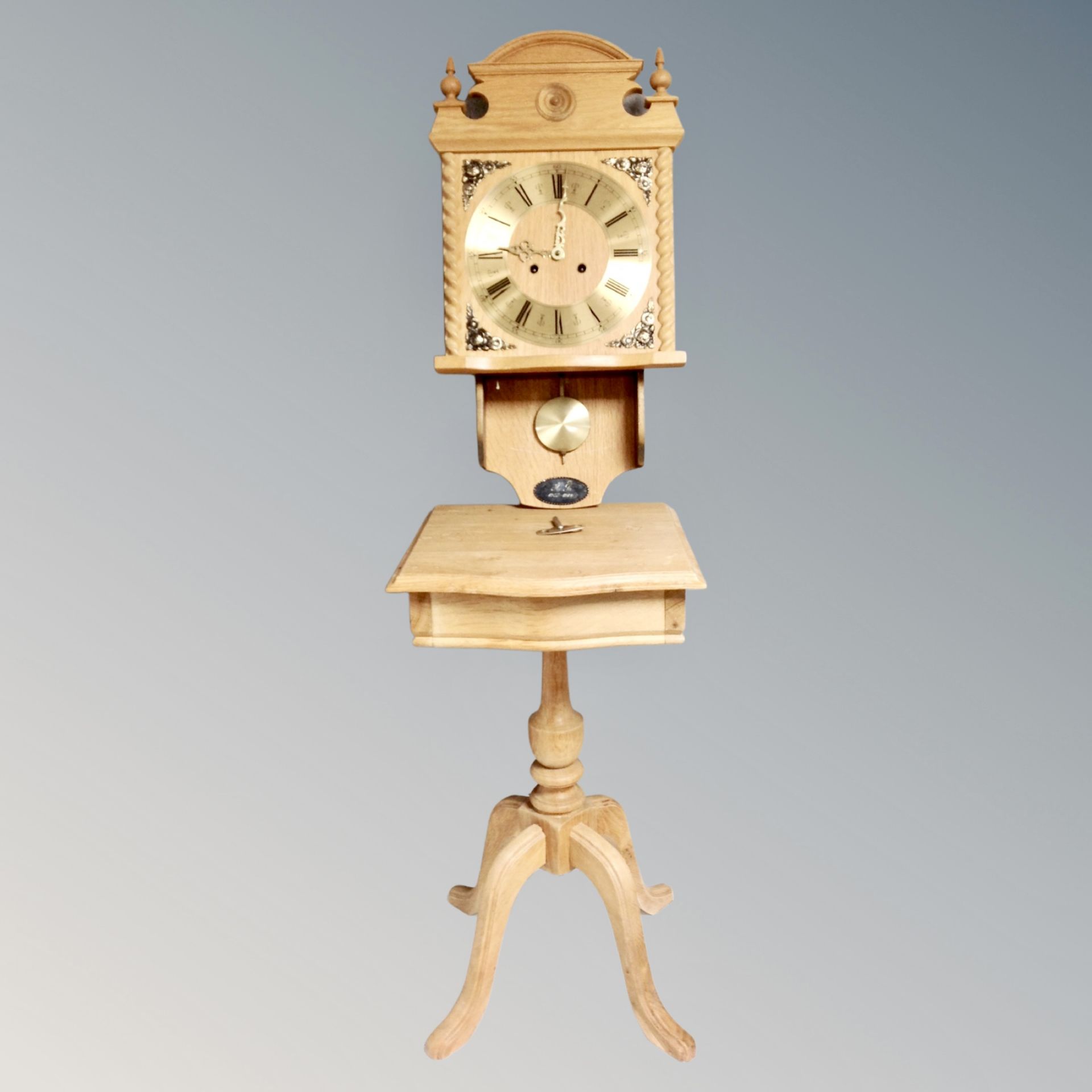 A Genfa blond oak wall clock with pendulum and key together with a further blond oak pedestal table