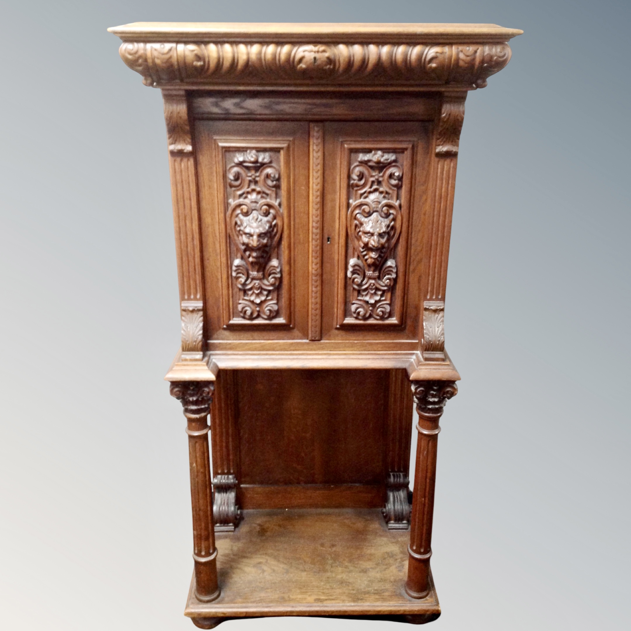 An early 20th century carved oak double door cabinet fitted a drawer on raised pillar legs