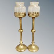 A pair of brass ecclesiastical candlesticks with glass shades,