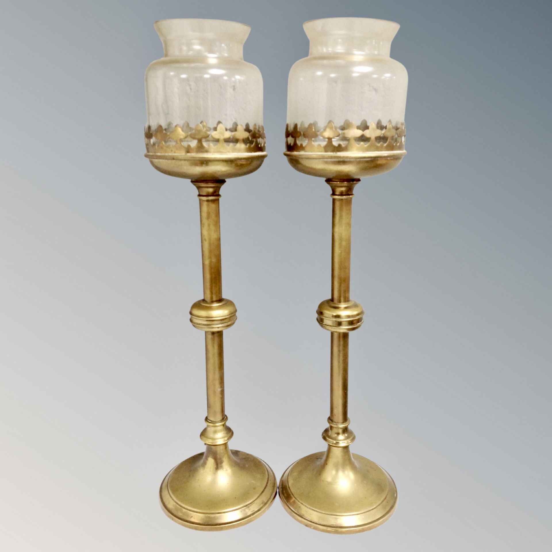 A pair of brass ecclesiastical candlesticks with glass shades,