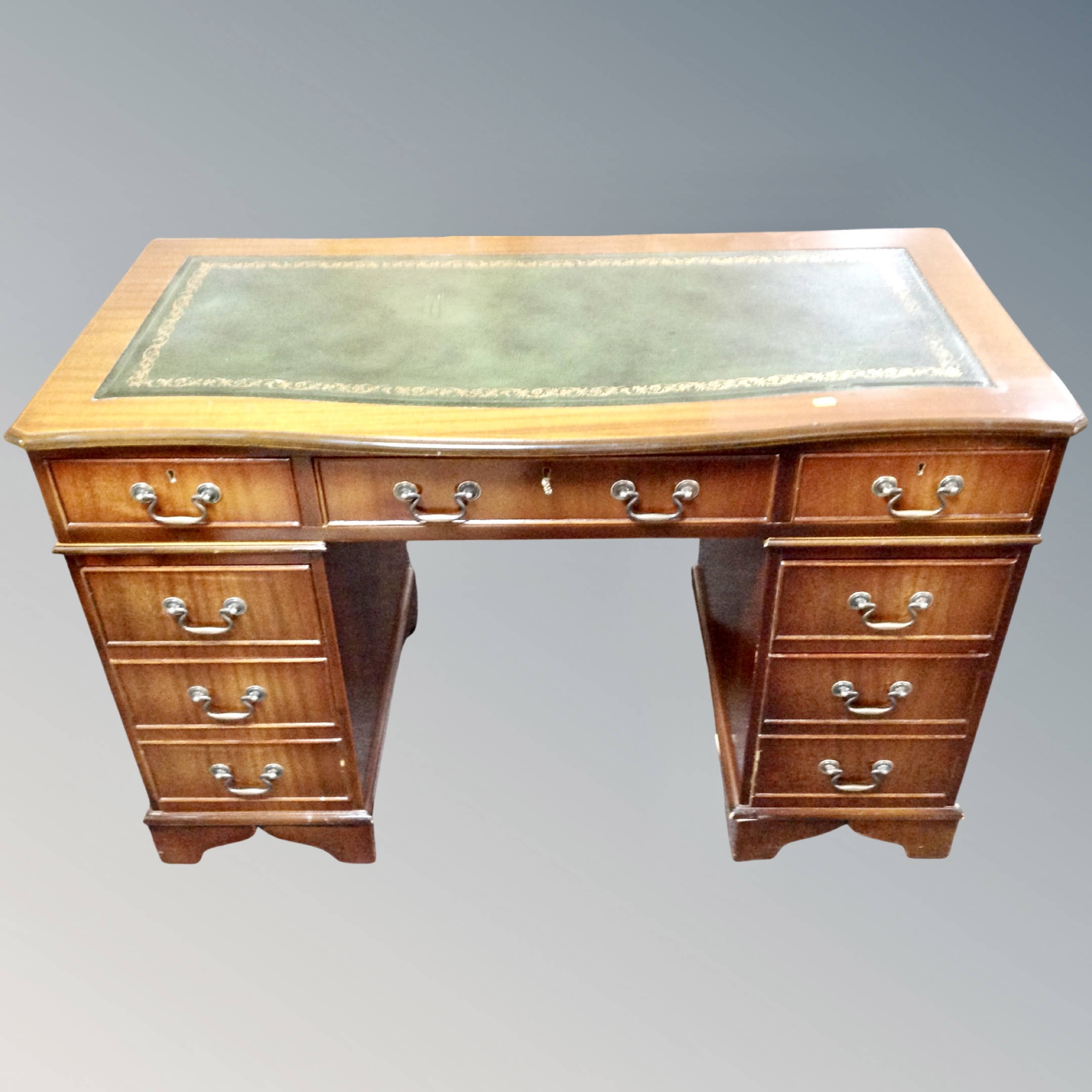 A Georgian style serpentine fronted writing desk fitted with nine drawers and green leather panel