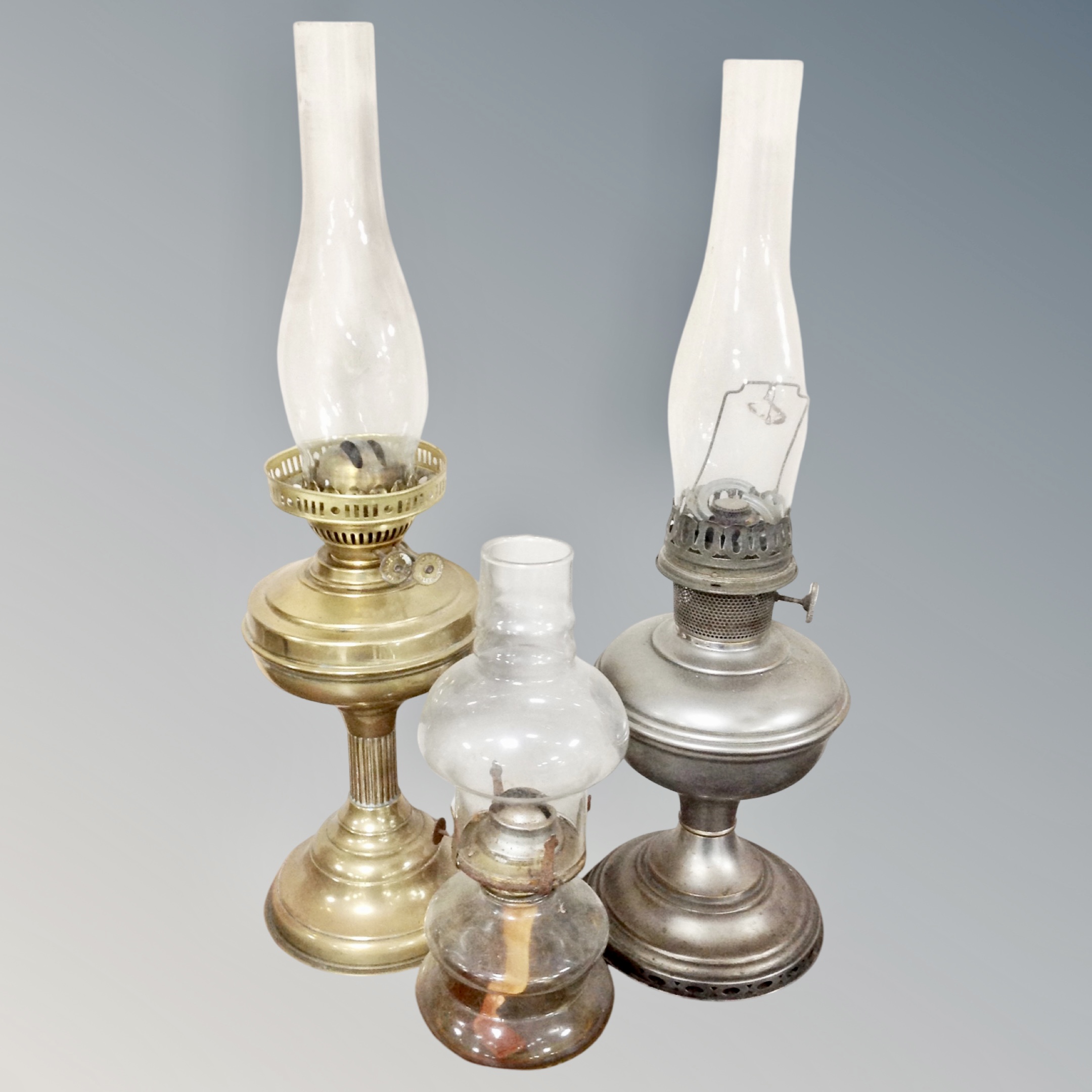 A Victorian brass oil lamp with cranberry glass reservoir together with three further oil lamps in