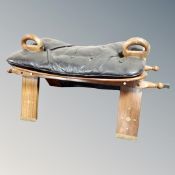 A hardwood brass inlaid camel stool with black leather saddle