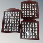 Three display cases containing a collection of china and metal thimbles