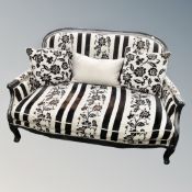 A French style ebonised salon settee in black and grey floral fabric with loose cushions