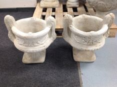 A pair of concrete twin handled classical urns on stands