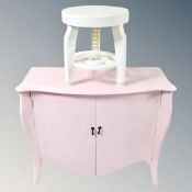 A serpentine fronted pink double door cabinet together with a circular plastic stool