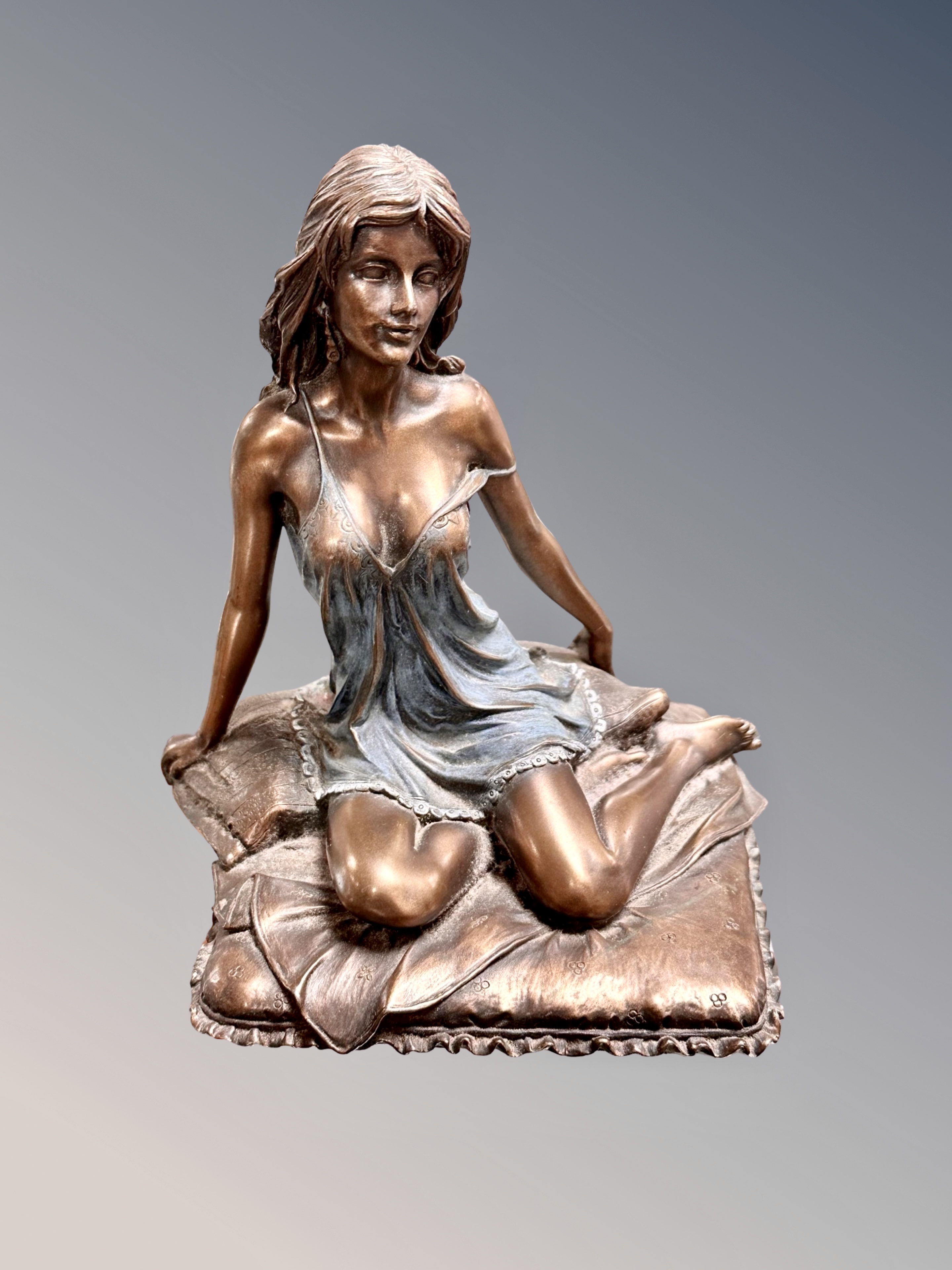 A bronzed figure of a scantily dressed female seated on cushions