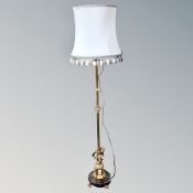 A brass figural cherub standard lamp on circular brass base and paw feet with silk tasseled shade