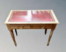 A pine two drawer writing table with red tooled leather inset panel on raised legs