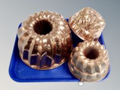 Three copper-finish jelly moulds, largest 27 cm in diameter.