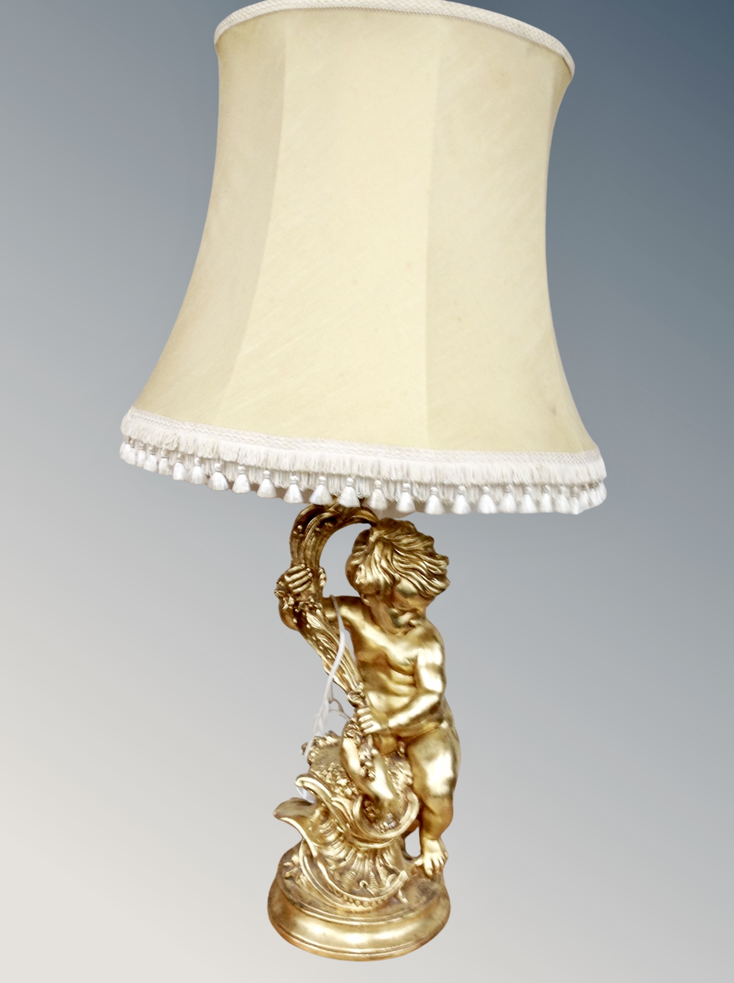 A gilt chalk cherub figural table lamp with tasselled shade