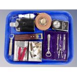 A tray containing vintage tape measure, hip flask, bottle openers, Swiss army knives, Bayer lighter,