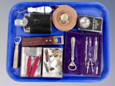 A tray containing vintage tape measure, hip flask, bottle openers, Swiss army knives, Bayer lighter,