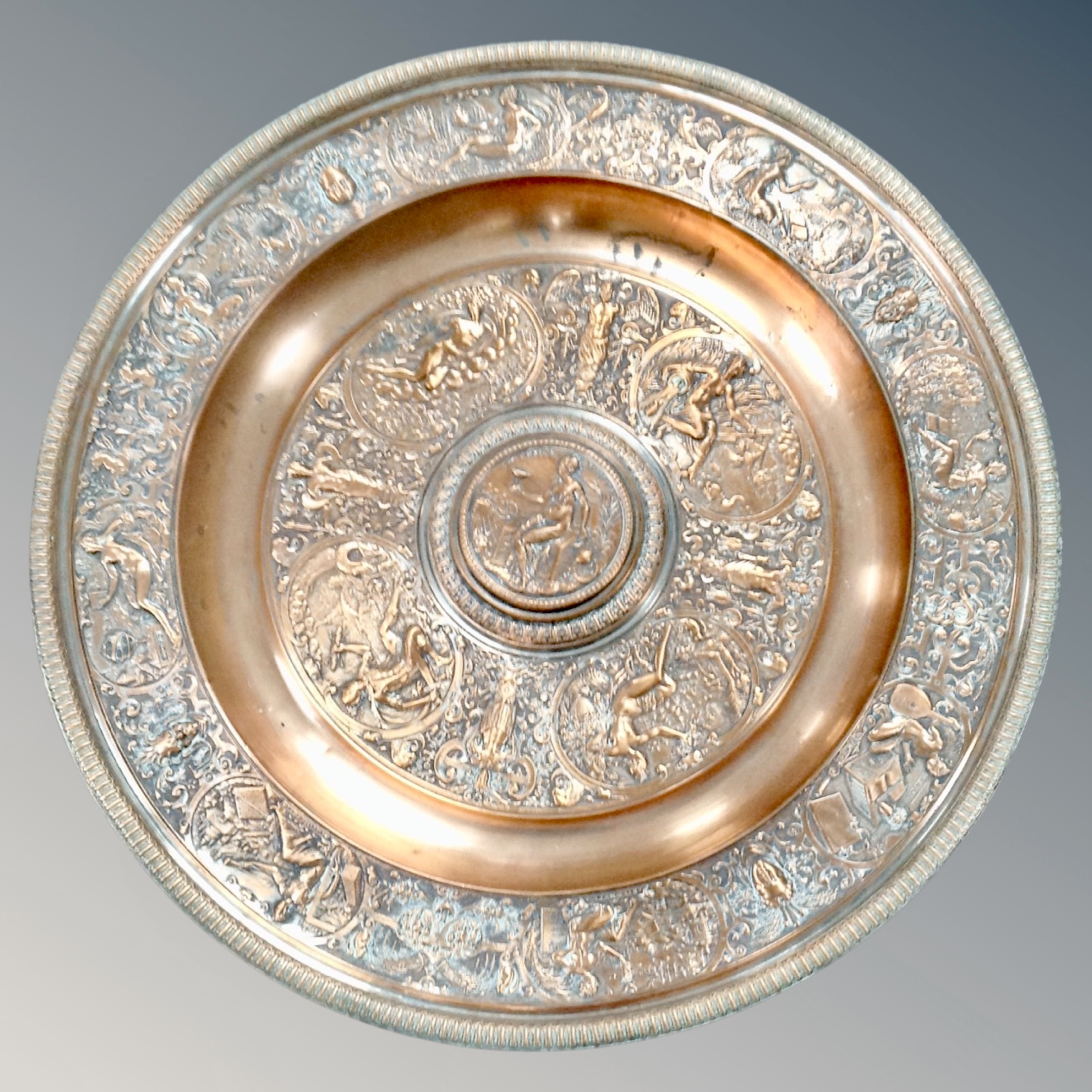 An ornate copper plate on pewter charger,