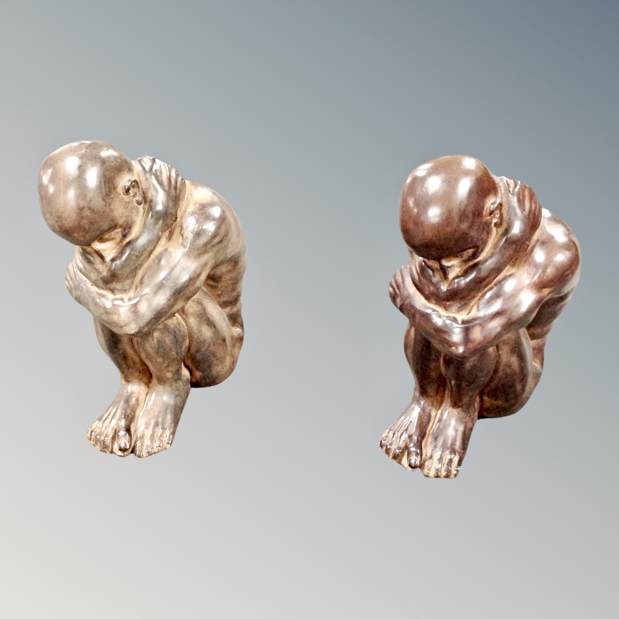 A pair of contemporary resin figures of seated male nudes,