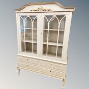 A cream and gilt bookcase with four drawers beneath,