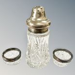 A silver topped sugar sifter together with a pair of silver rimmed salts.