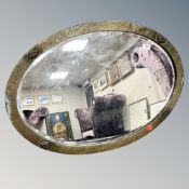 An Arts & Crafts hammered brass oval mirror, width 83 cm.