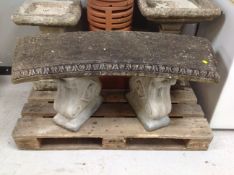 A weathered concrete shaped garden bench on classical pedestal