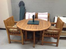 A circular teak garden table, four slatted back armchairs with cushions,