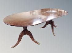 A mahogany oval twin pedestal dining table with leaf on brass capped feet