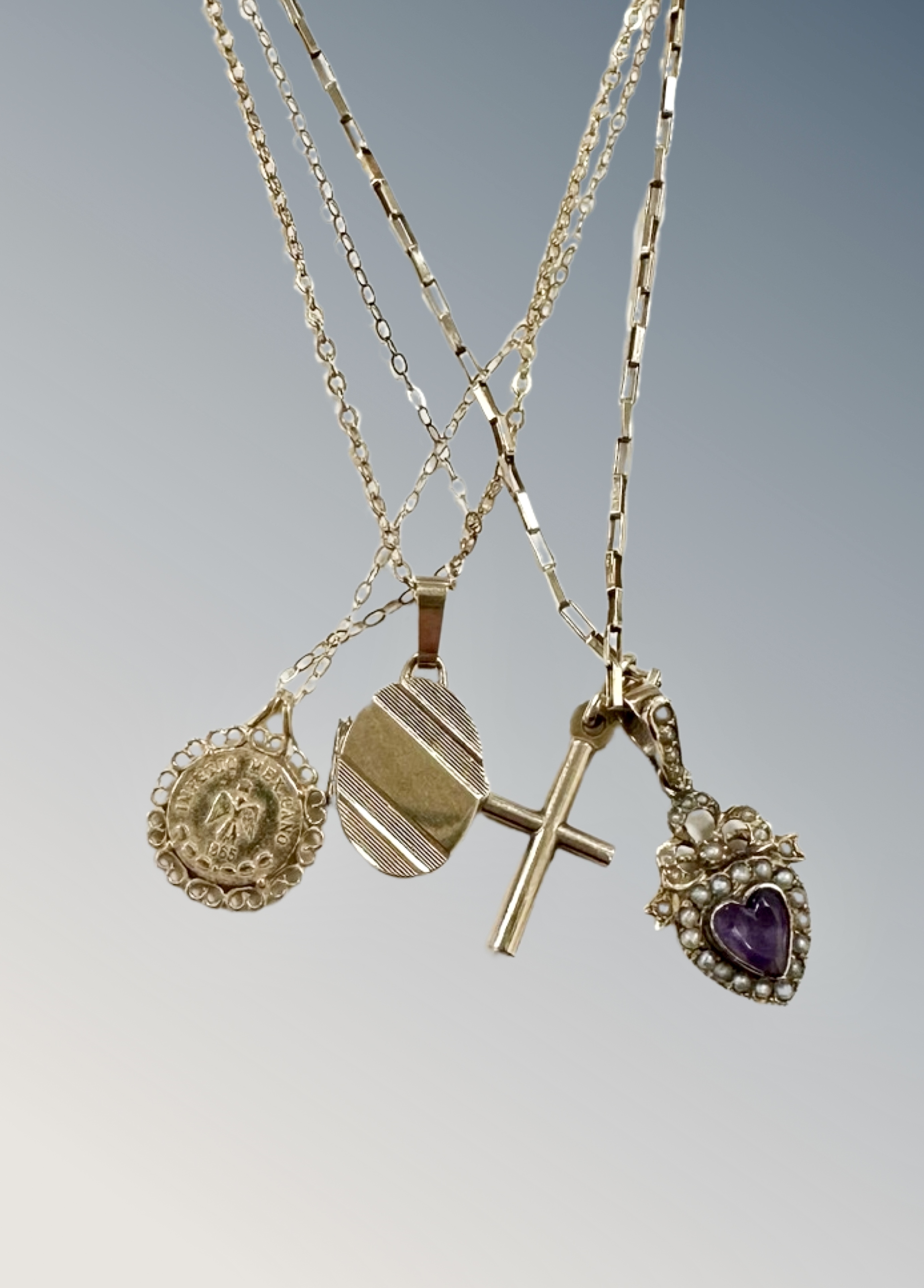 A 9ct gold chain holding a crucifix pendant and a further heart-shaped amethyst and seed pearl