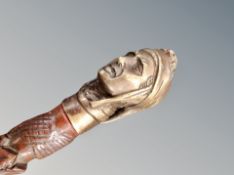 A heavily carved walking stick with brass figural pommel