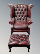A Chesterfield oxblood buttoned leather wing backed armchair and matching footstool